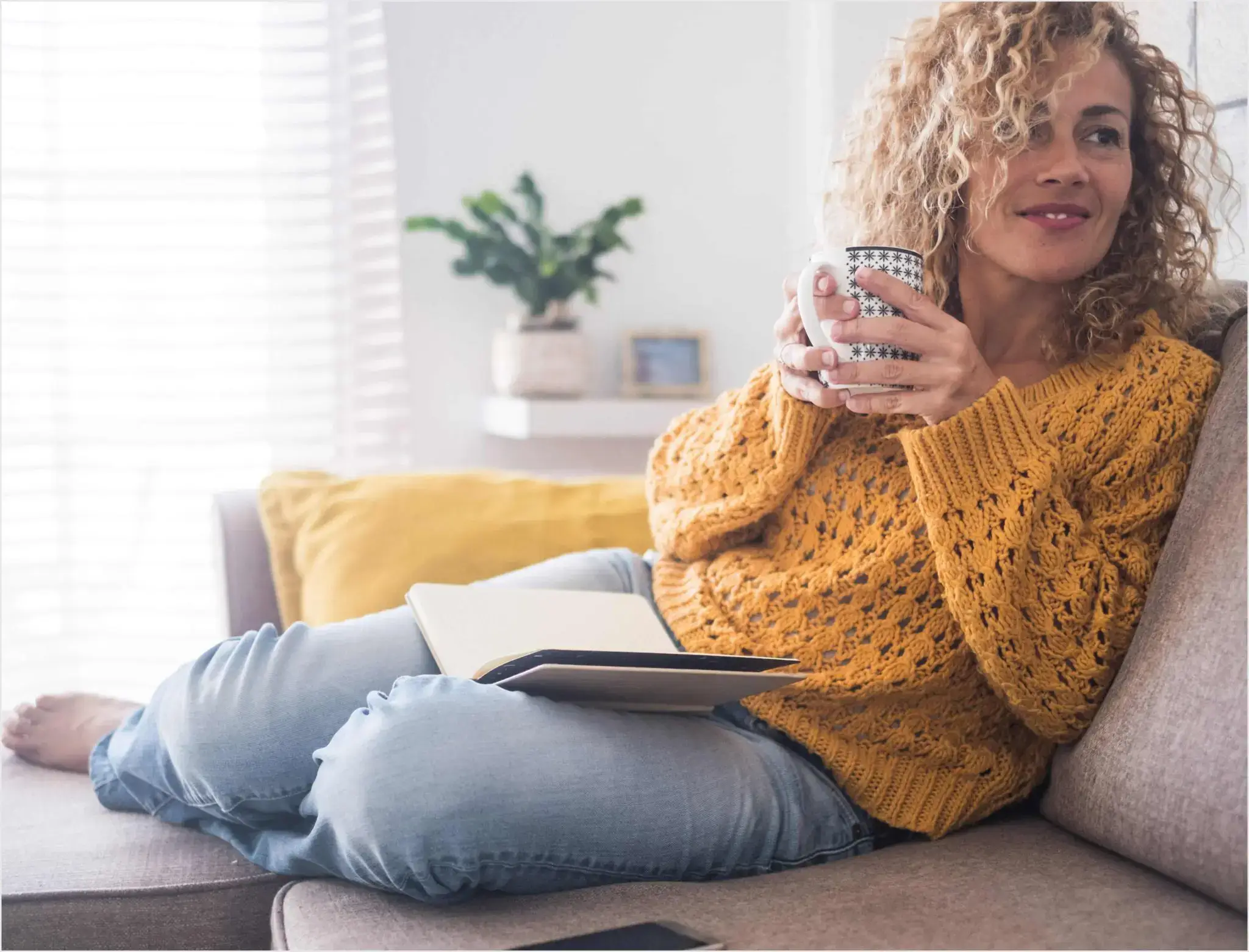 Woman on her couch at home with a notebook in her lap and a mug in her hands
